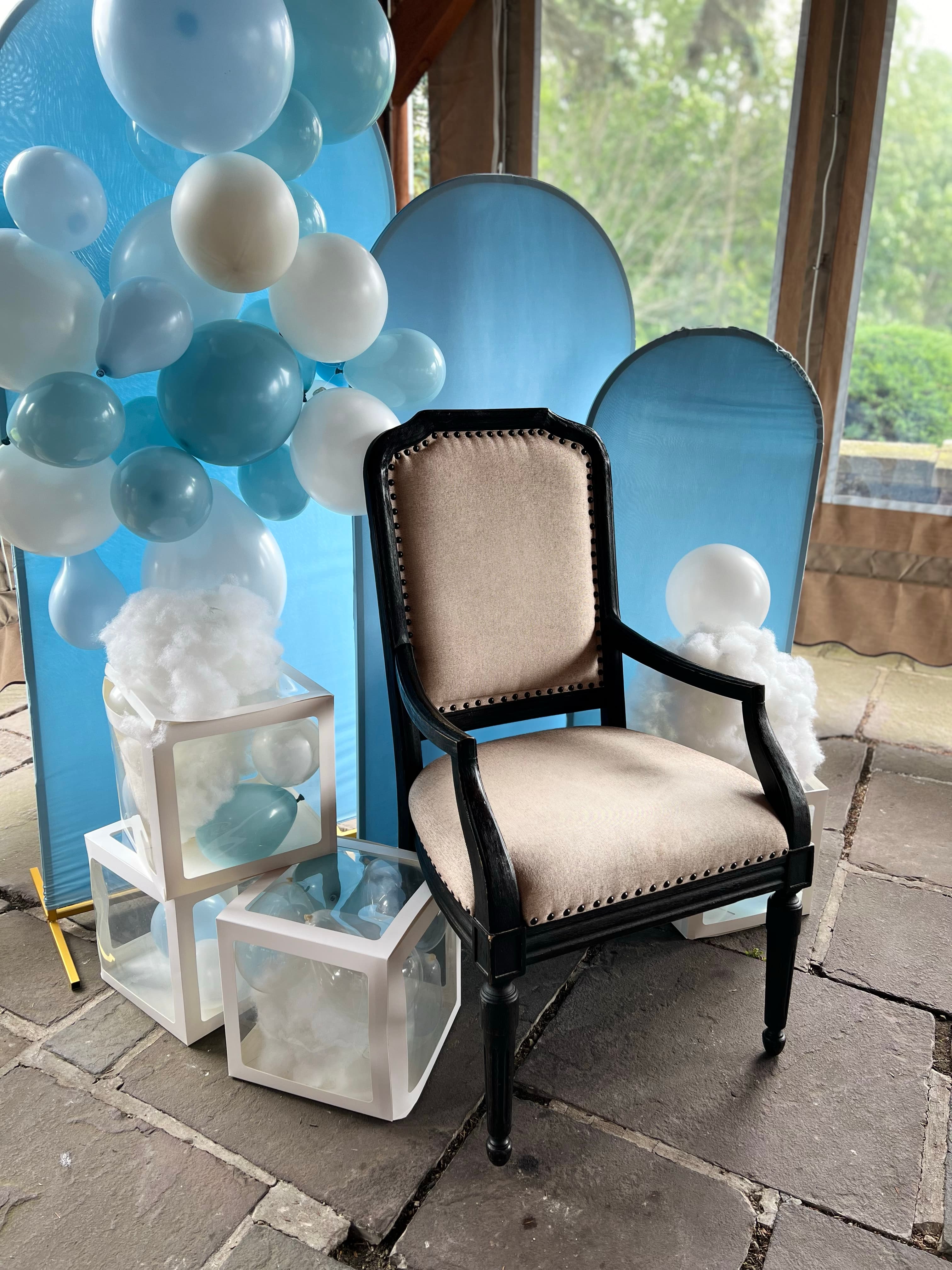 A decorated area for a baby shower with a chair, balloons, and baskets with balloons and cloud type decorations.