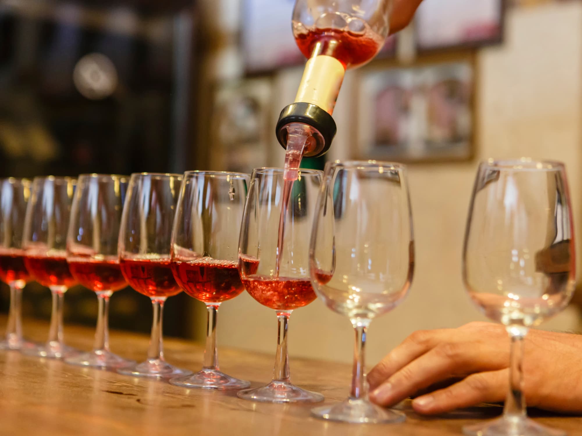 A hand pours wine into a row of empty glasses.