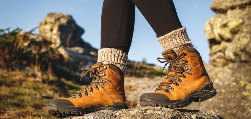 A person stands on a rocky surface, wearing brown hiking boots and black leggings with knit leg warmers.