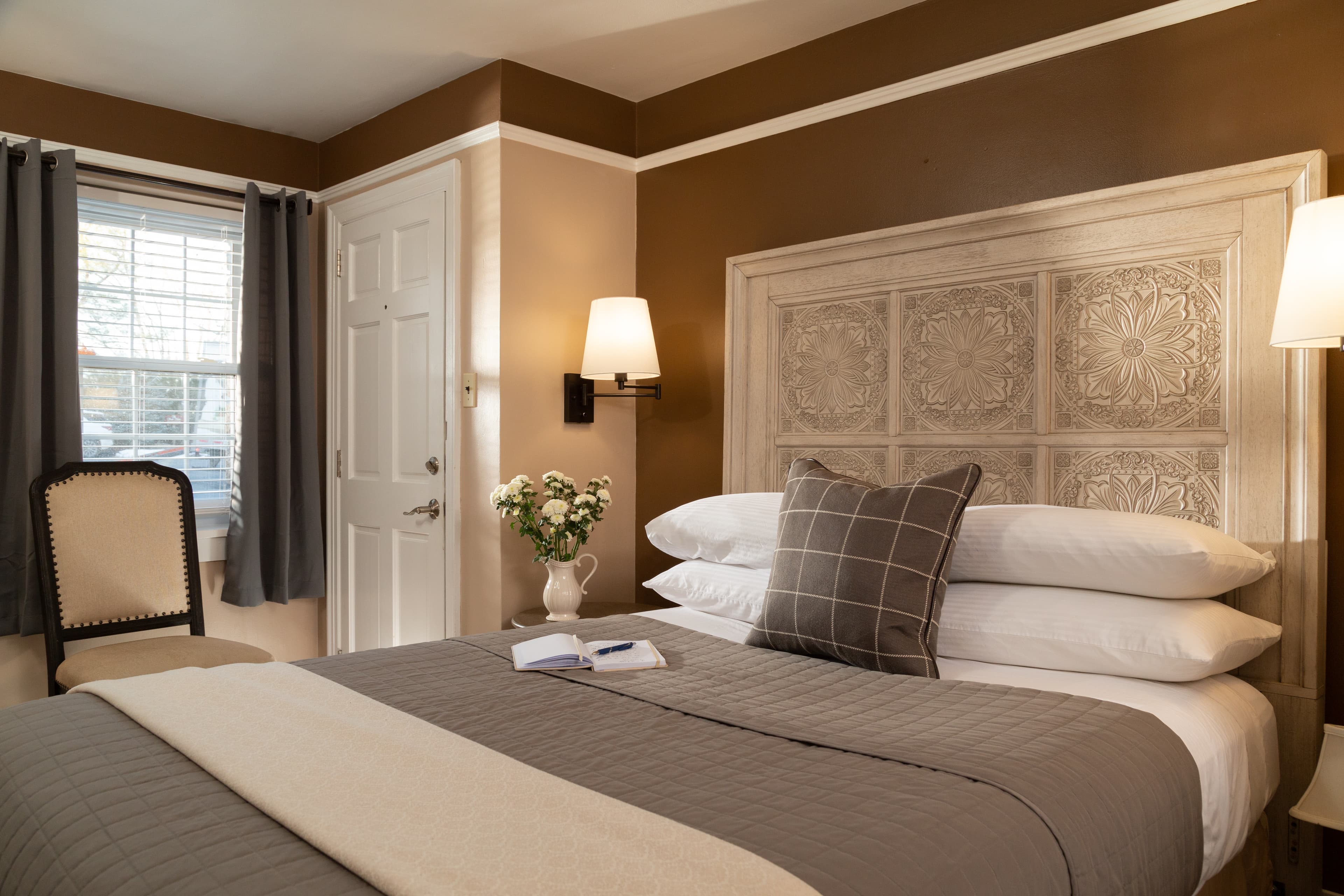 Cozy bedroom featuring a neatly made bed, decorative pillows, a vintage chair, and elegant wall art.