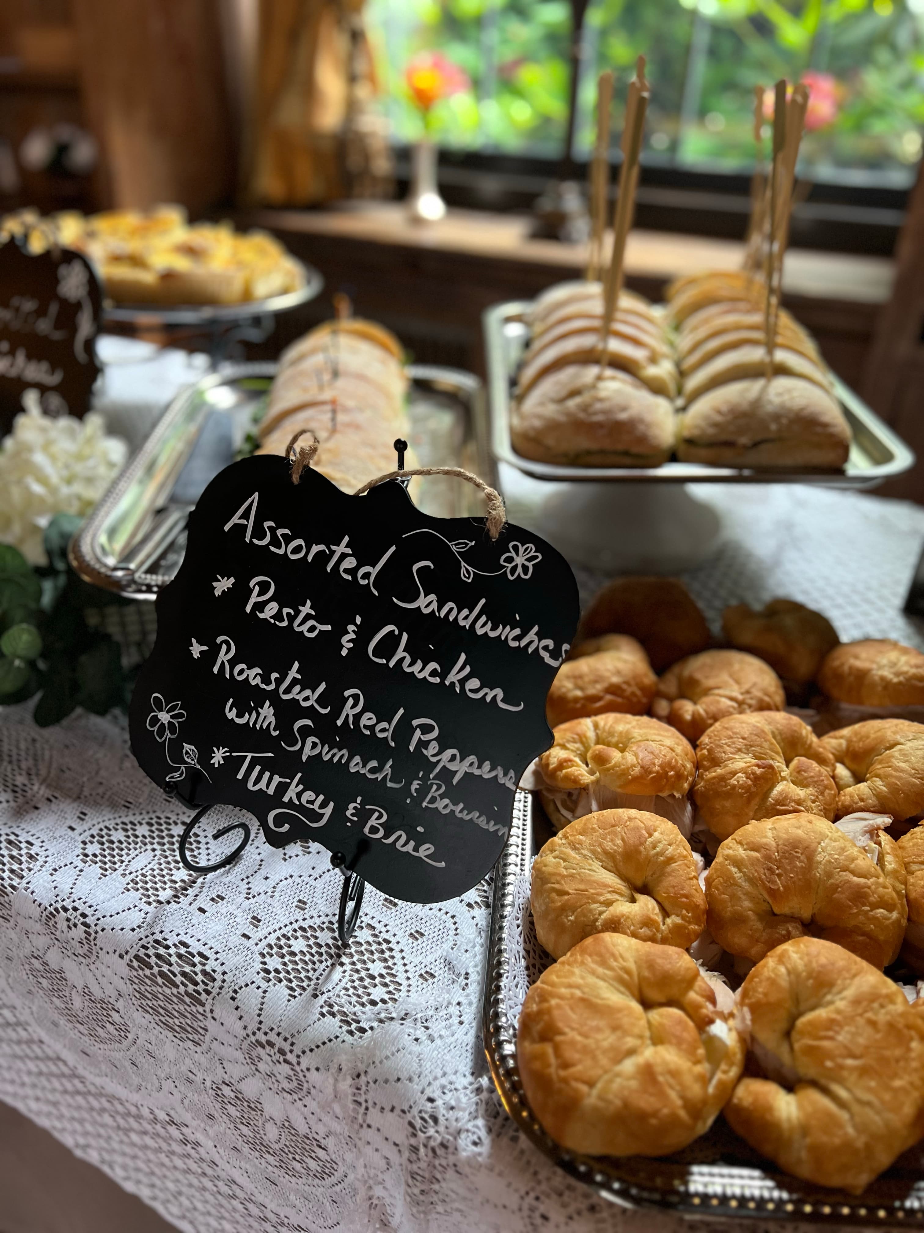 A buffet table with assorted sandwiches, including pesto and chicken, roasted red pepper, and turkey and brie.