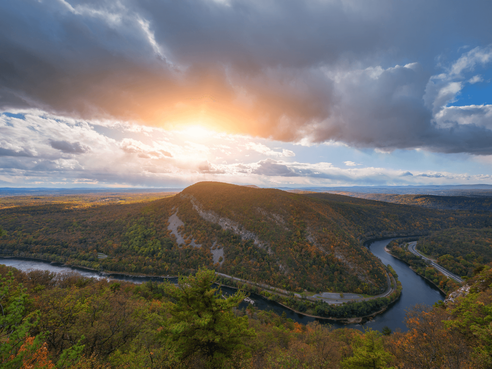A panoramic view of a vibrant, sunlit landscape featuring rolling hills and a winding river beneath a cloudy sky.