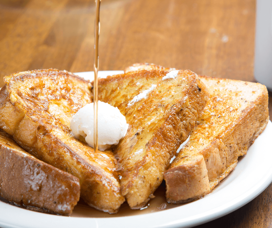 A plate of French toast with a dollop of butter and syrup drizzling over it.