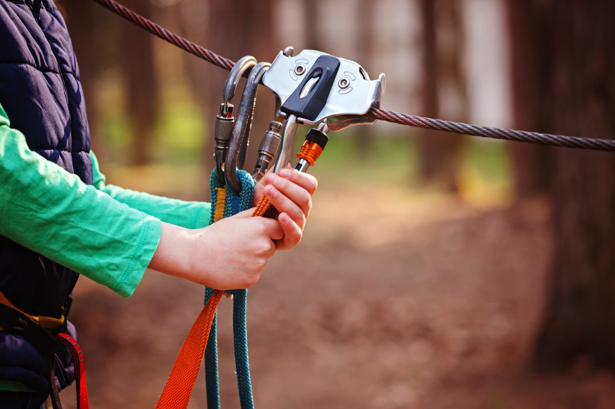 A person in a green shirt grips climbing gear attached to a cable in a forest setting.