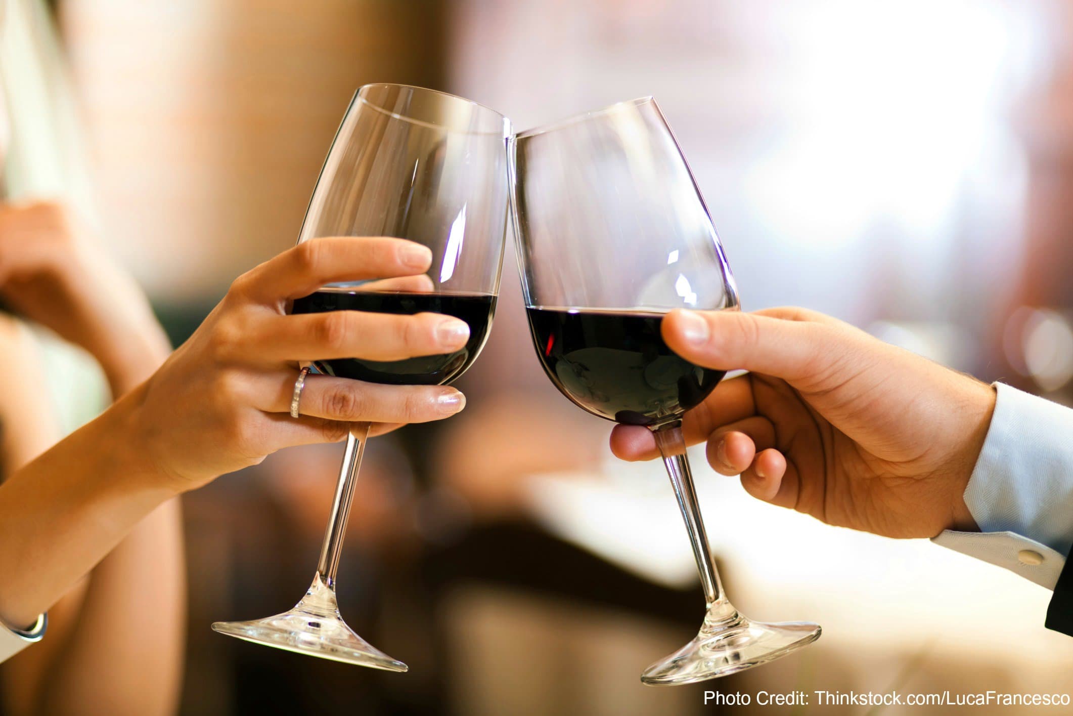 Two hands holding wine glasses, toasting with red wine.