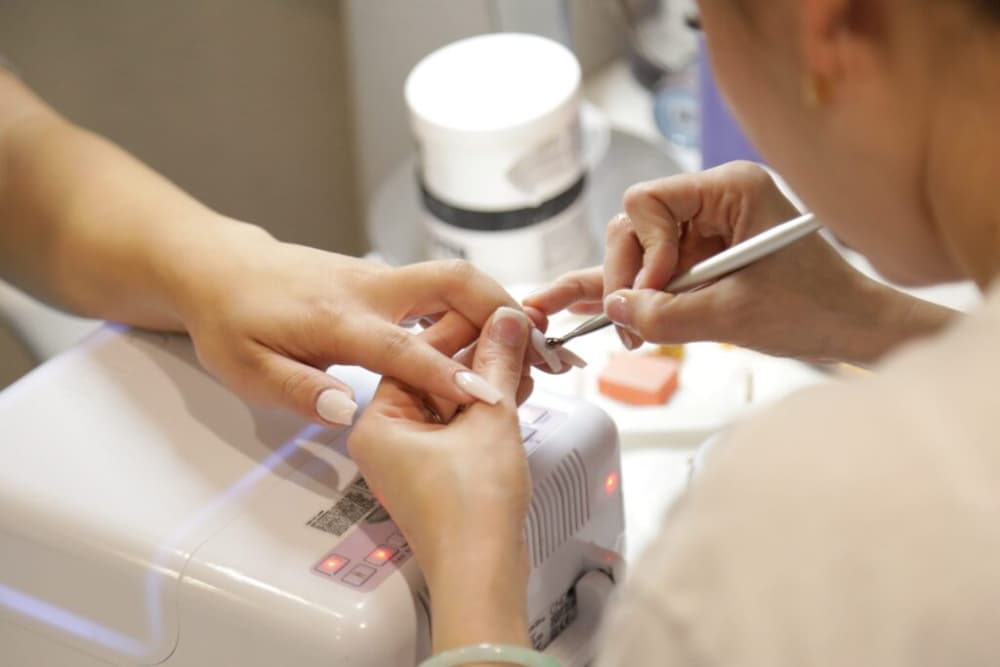 A woman getting her nails painted by a nail tech in a salon