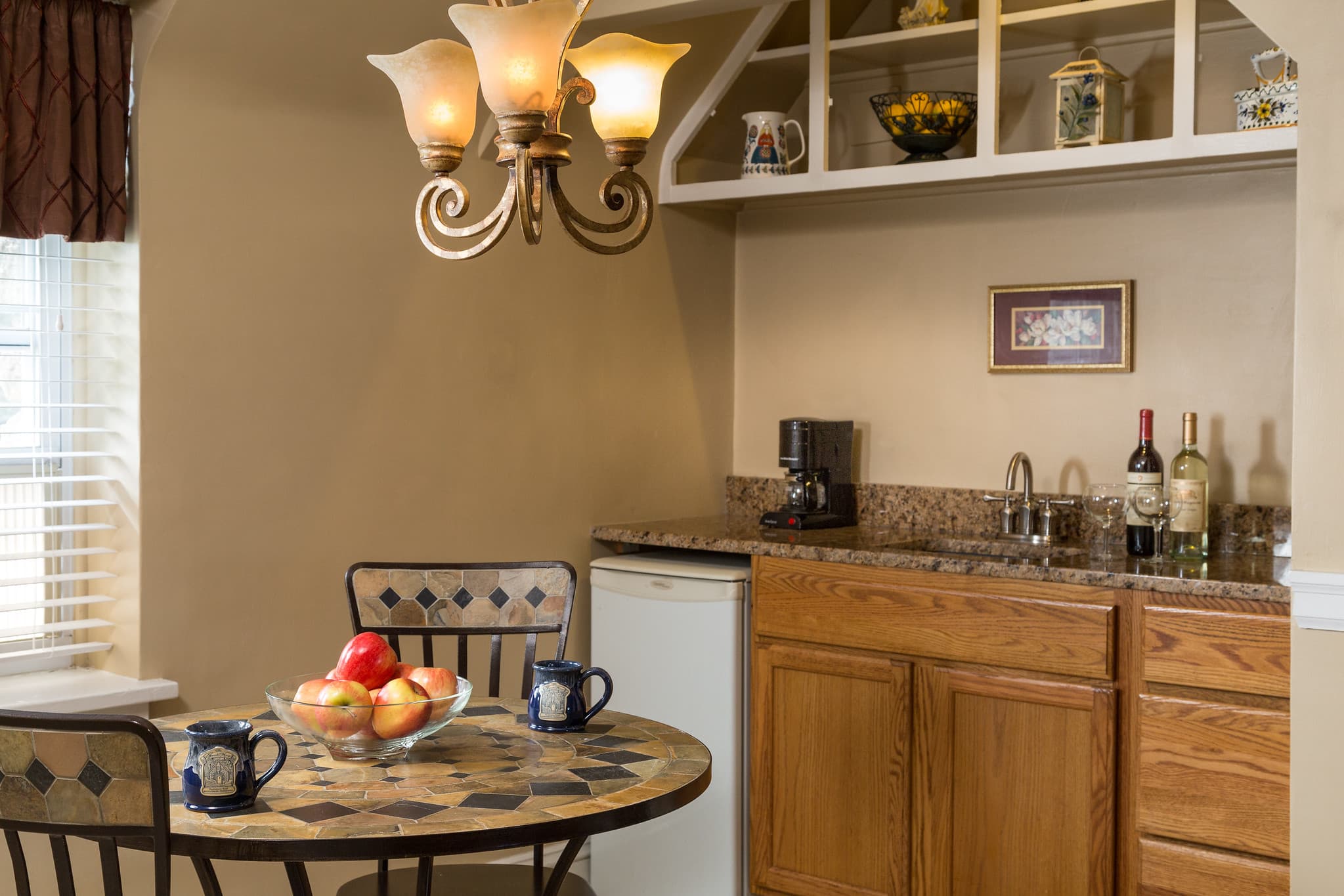 Cozy kitchen with a mosaic table, fruit bowl, and a well-organized countertop featuring a coffee maker and wine.