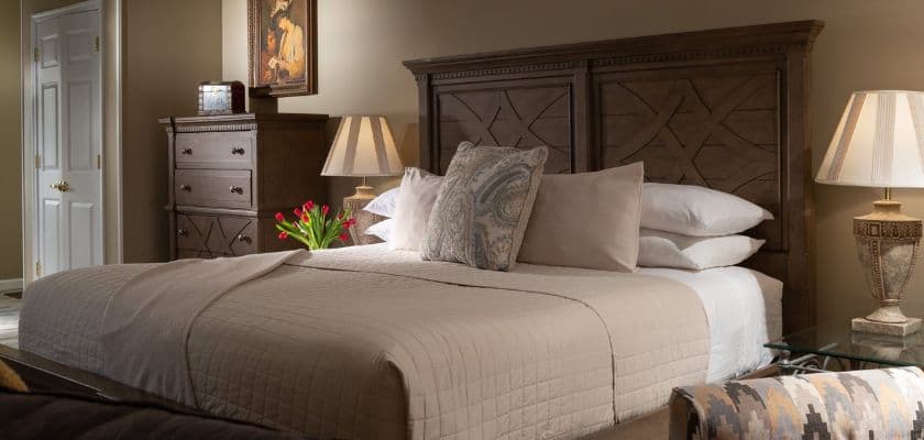 A cozy bedroom featuring a queen-sized bed, decorative pillows, a bedside table with a lamp, and a vase of tulips.