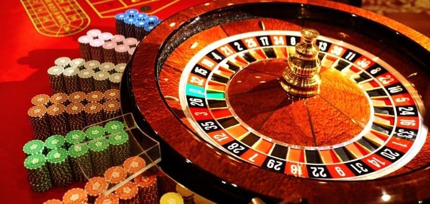 A roulette wheel and colorful stacks of poker chips on a casino table.