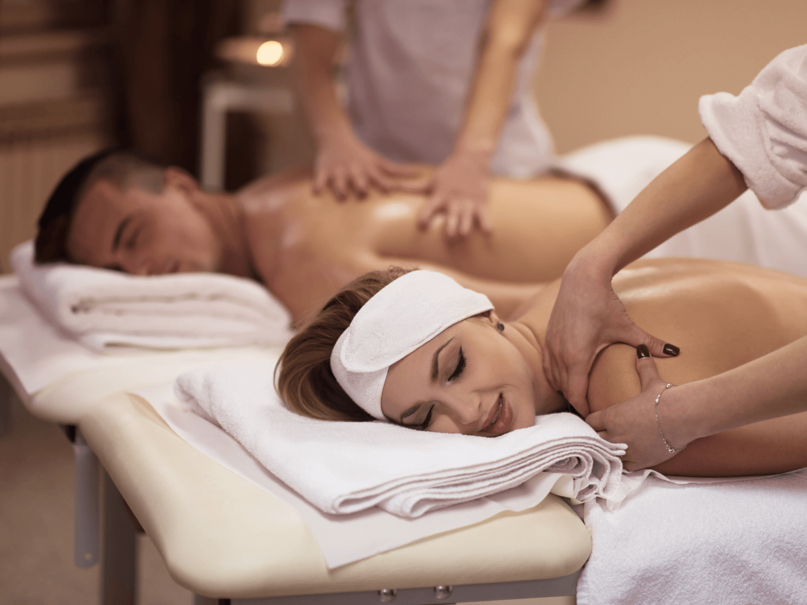 A woman and a man receive relaxing massages on adjacent tables in a serene spa setting.