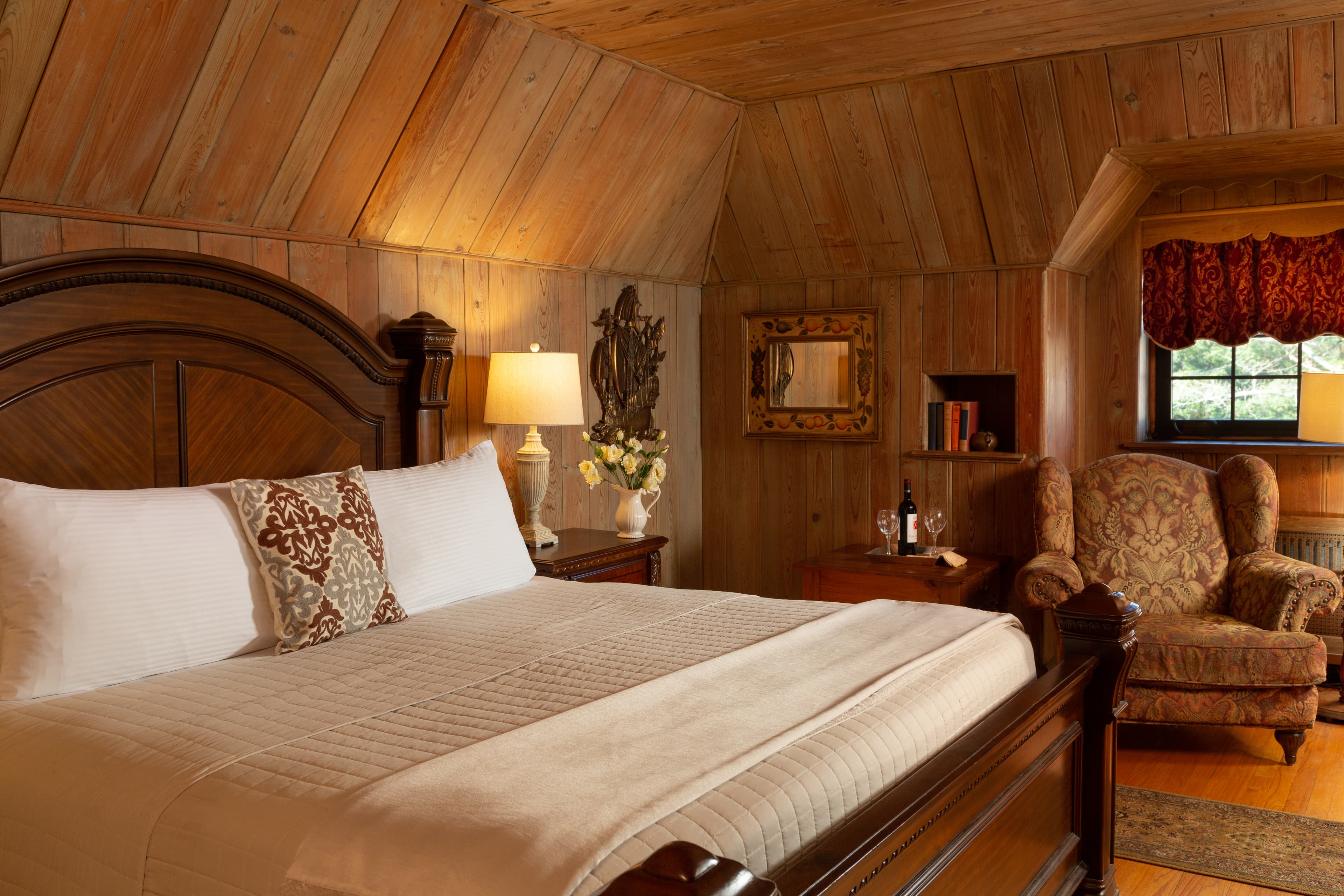 Cozy wooden-paneled bedroom featuring a large bed, armchair, and warm lighting.