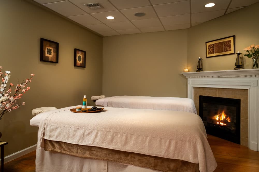 A relaxing spa room with two massage tables, a fireplace, and candles.