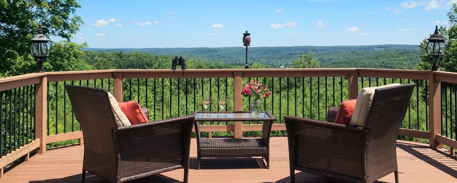 A cozy deck with two chairs and a table, overlooking a scenic green landscape under a blue sky.