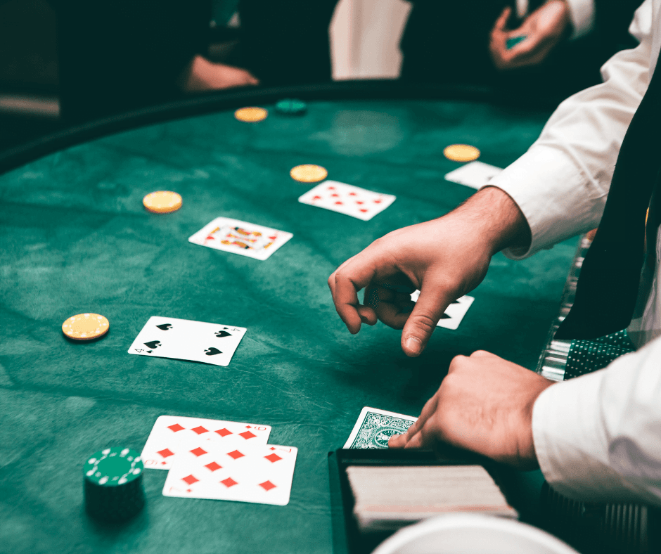 A hand reaches to place a card on a poker table with chips and playing cards scattered around.