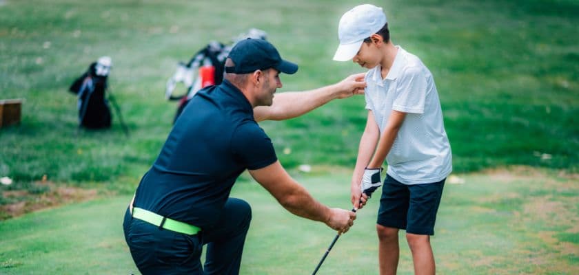 A golf instructor teaches a young boy the proper stance on the green.