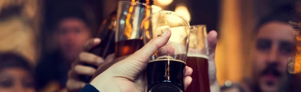 A group of people raising their glasses of beer in a toast, with a blurred background of a bar or pub.