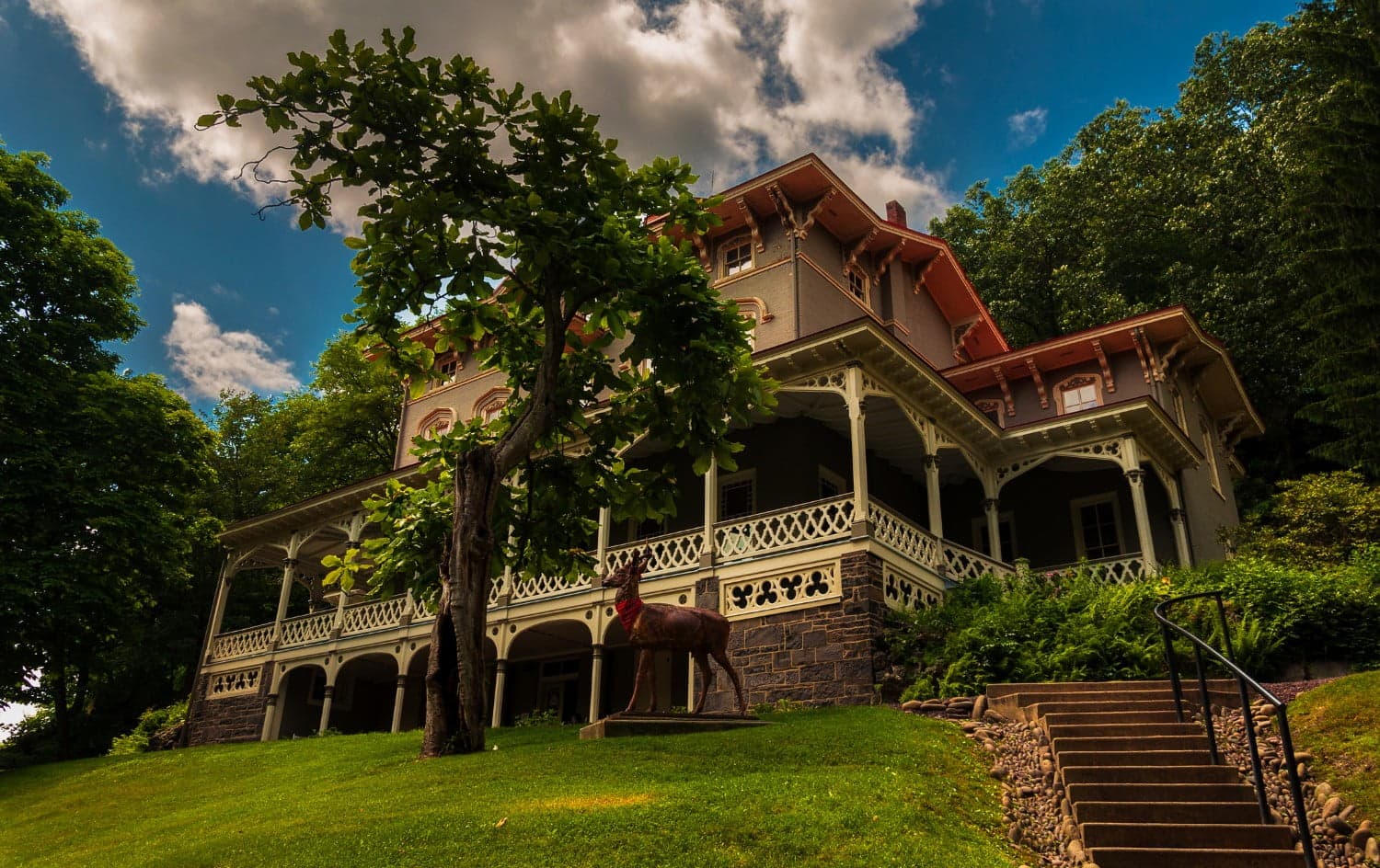 A historic mansion with intricate architectural details, surrounded by greenery and a sculpture of a horse.