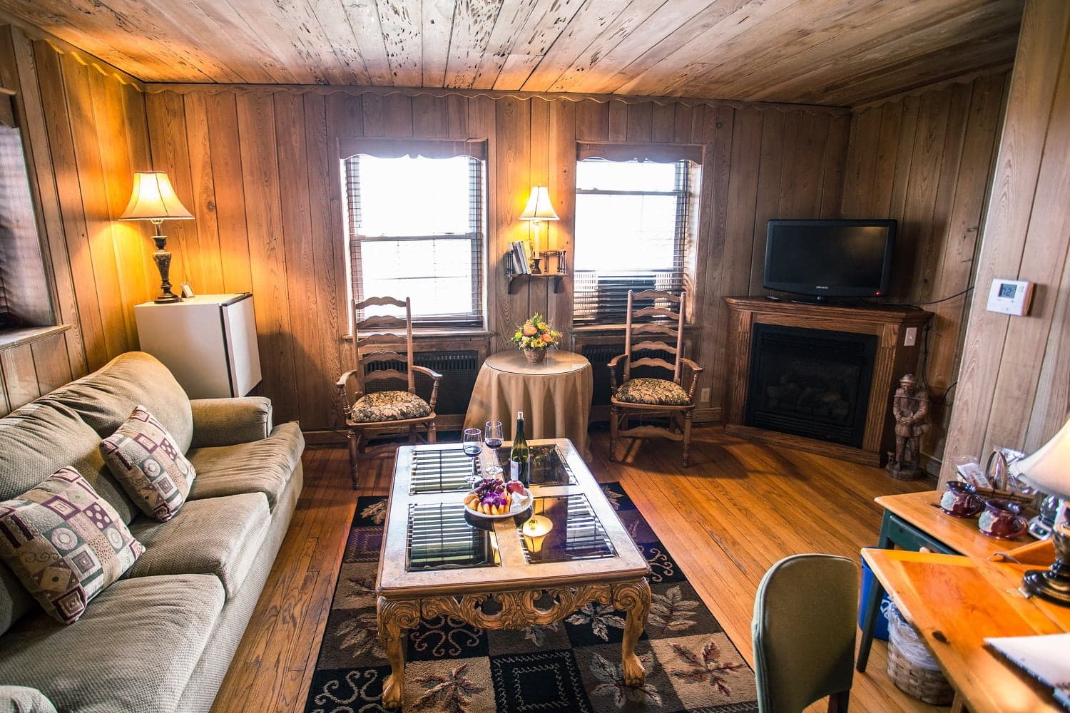 Cozy living room featuring wooden walls, a sofa, a table with fruit, and a television.