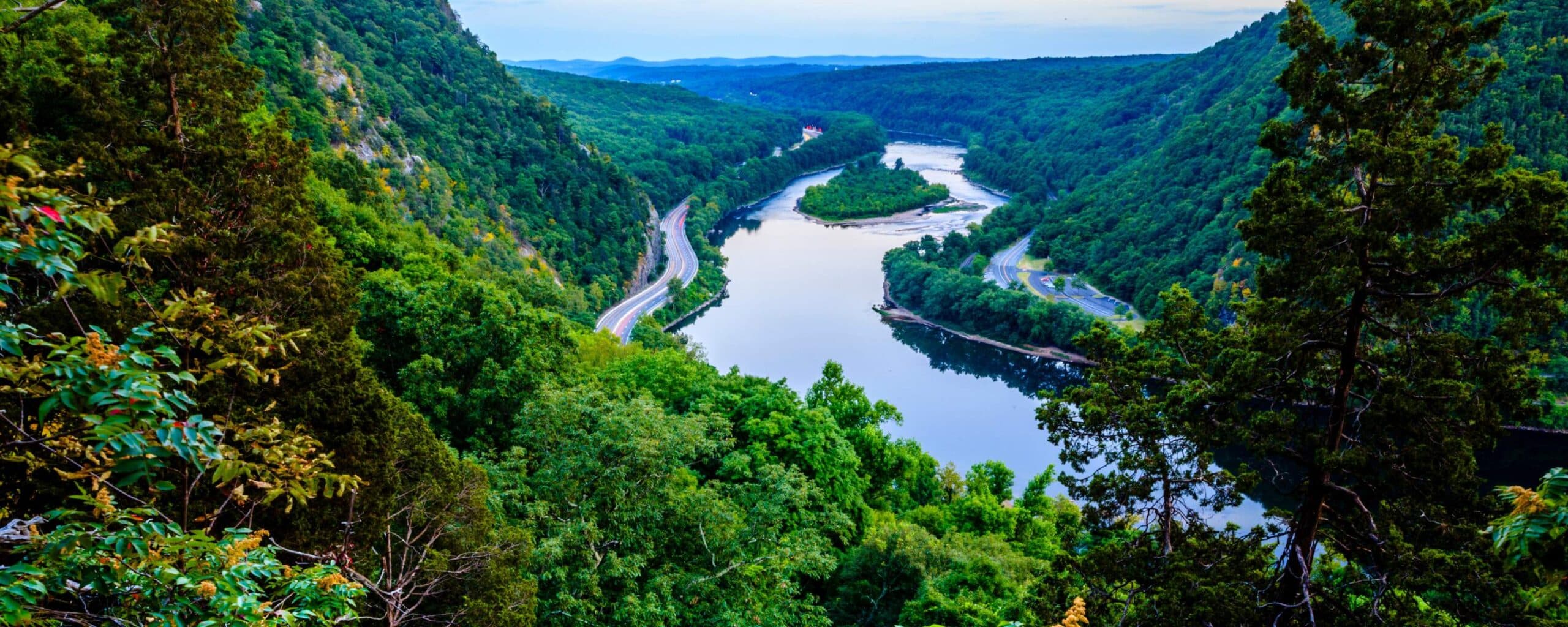 A serene river winding through lush green mountains under a blue sky.