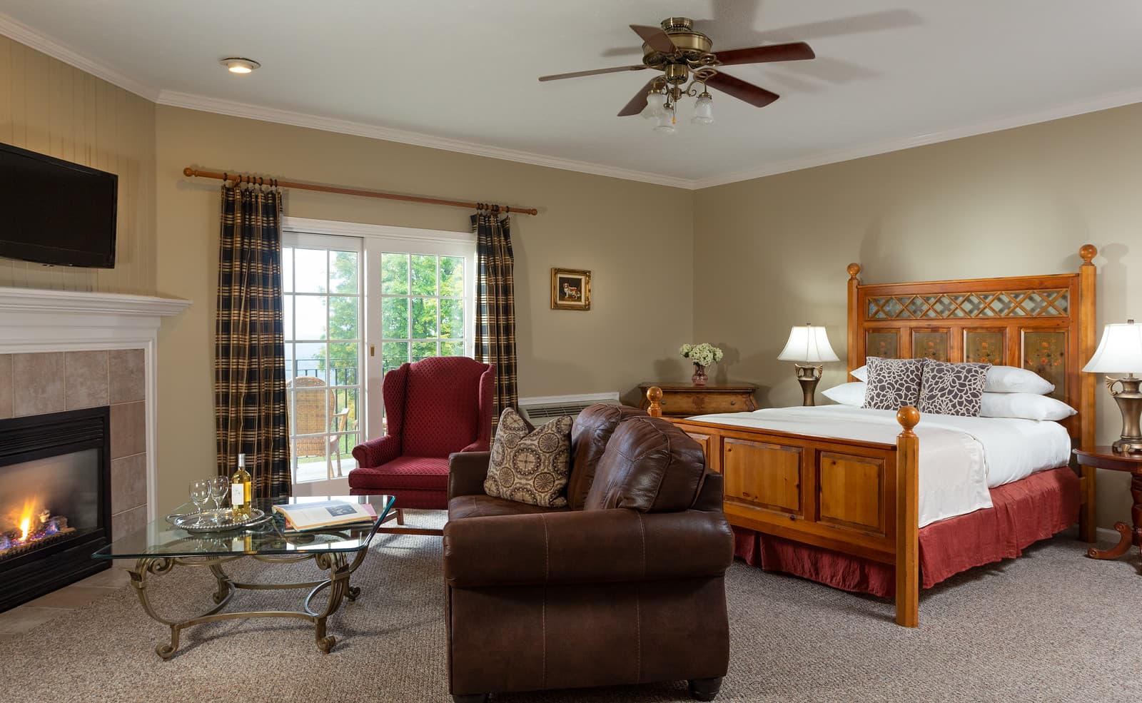 Cozy bedroom suite featuring a wooden bed, leather couch, and large windows leading to a patio.