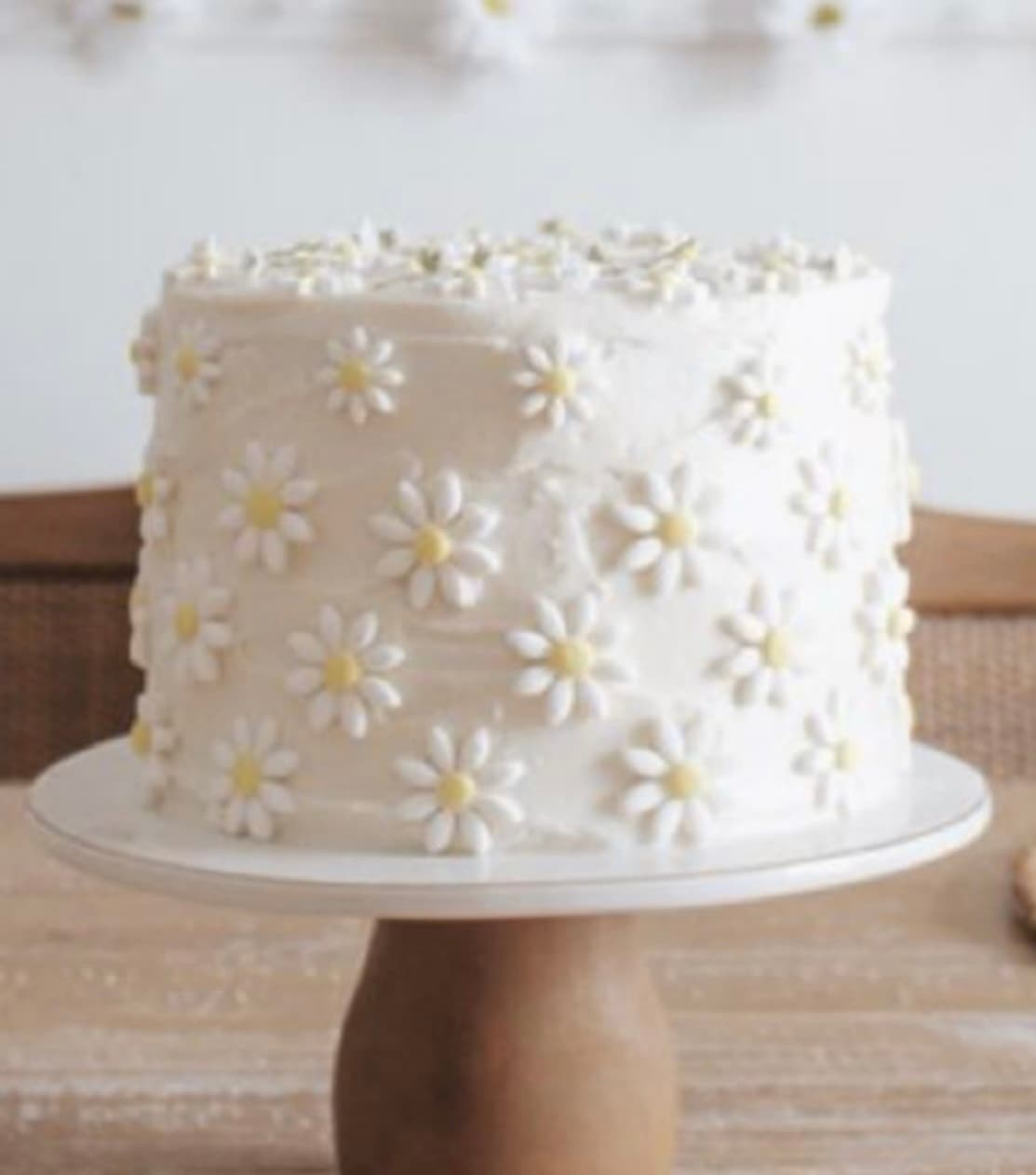 A round cake with white frosting and white daisies with yellow centers.