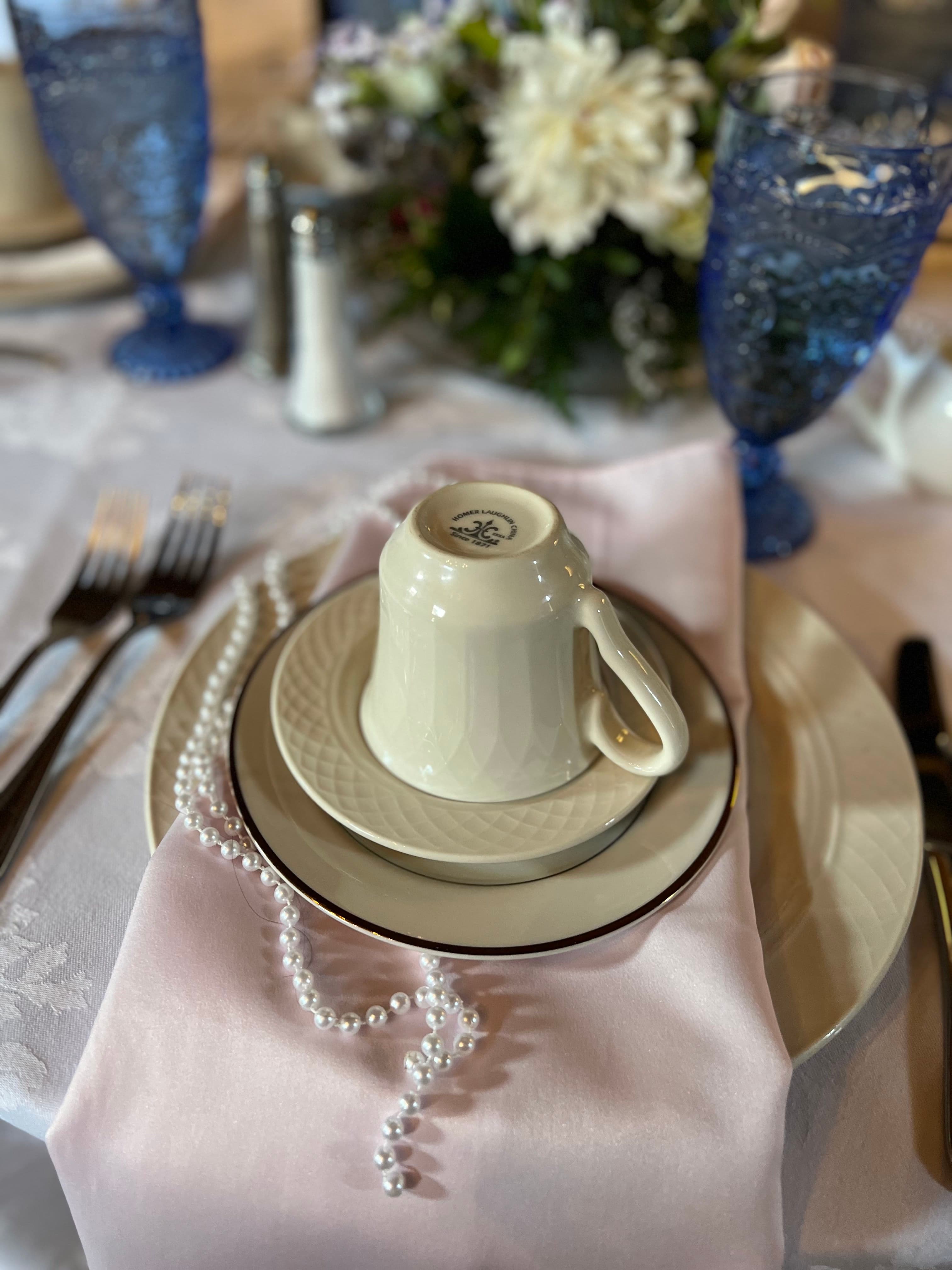 A beautifully set table setting with a teacup, saucer, plate, and pearl necklace.