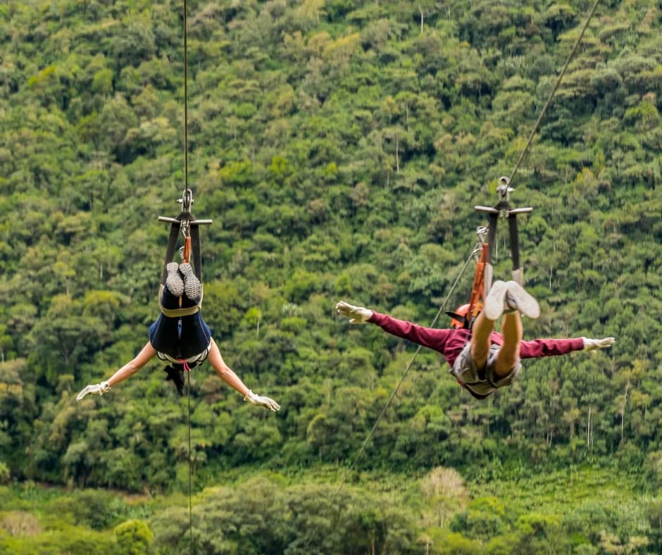 Two people zip-lining against a backdrop of lush green foliage.