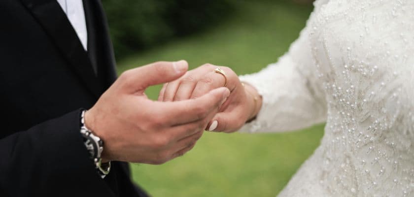 A close-up of a couple's hands during a wedding ceremony, showcasing a wedding ring on one hand.