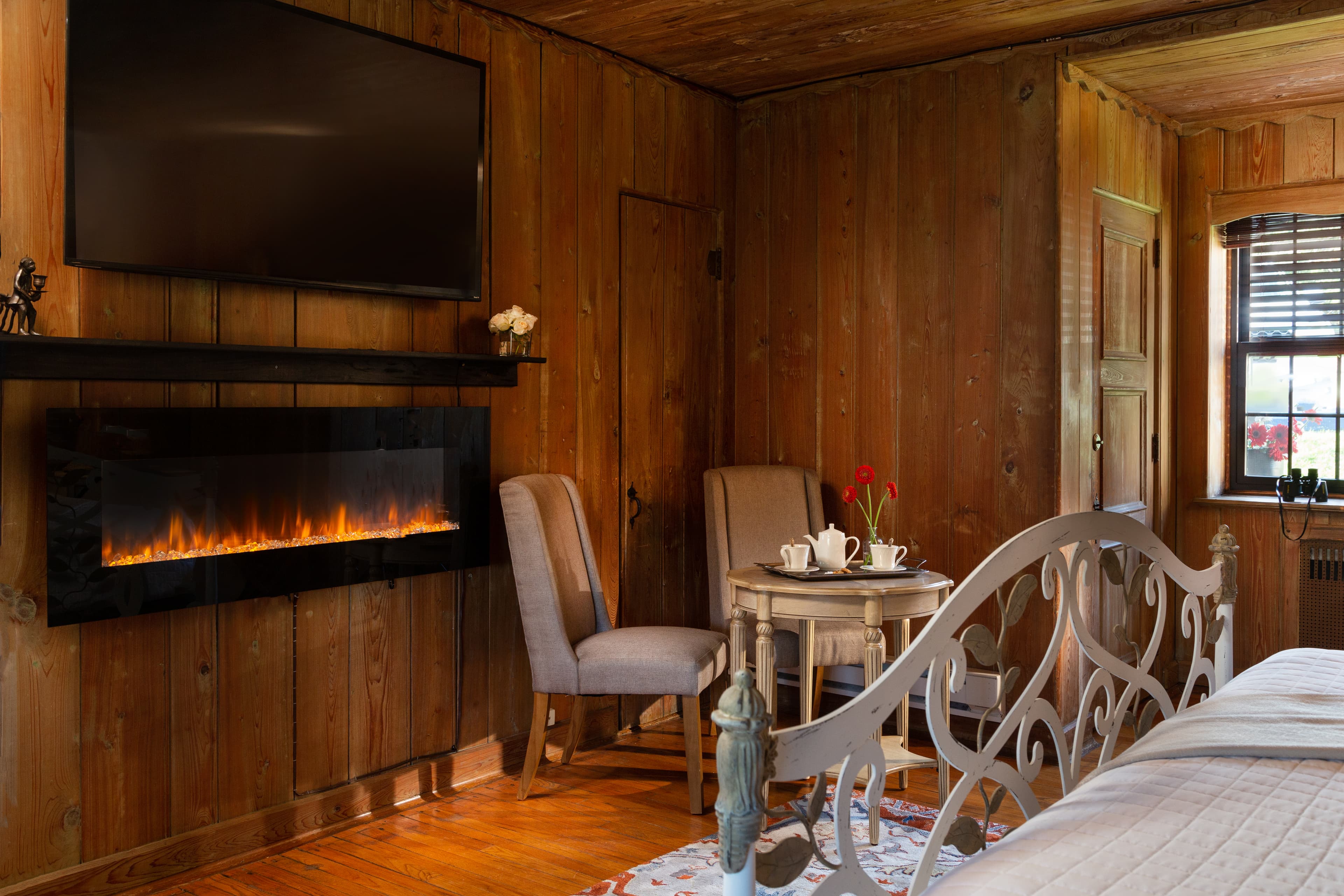 Cozy wooden room featuring a bed, seating area with a small table, and a mounted TV above an electric fireplace.