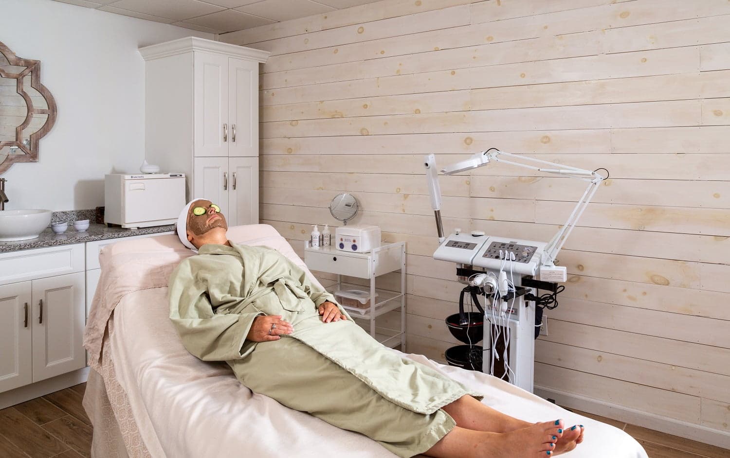 A person in a robe relaxes on a treatment bed in a spa-like room.