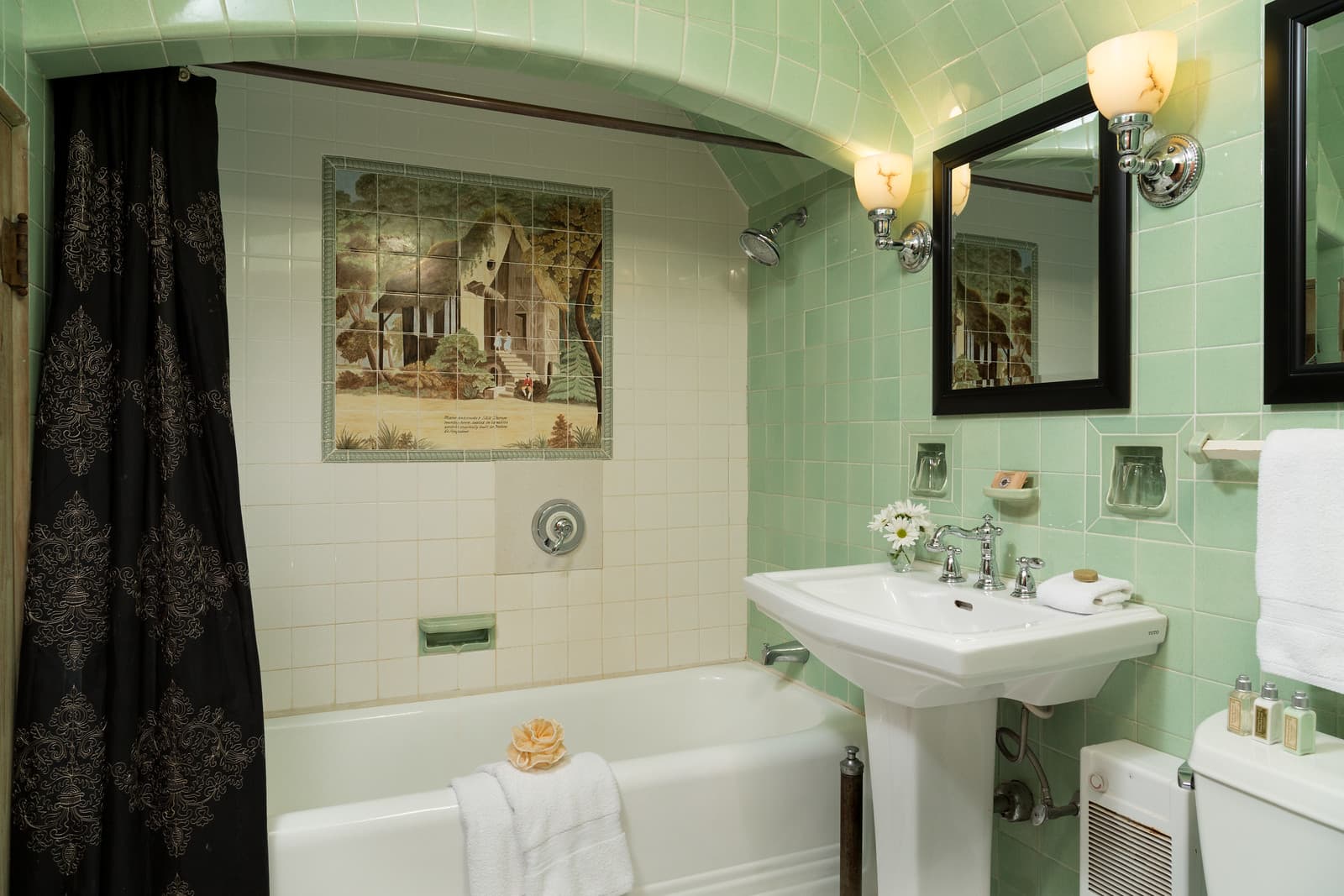 A vintage-style bathroom featuring mint green tiles, a shower-tub combination, and a decorative wall art.