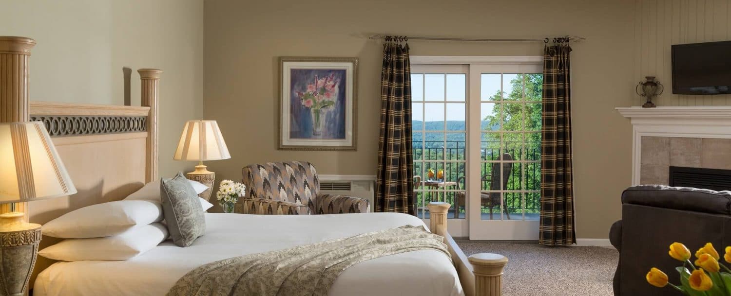 Cozy hotel room featuring a bed, armchair, art, and balcony doors with scenic views.
