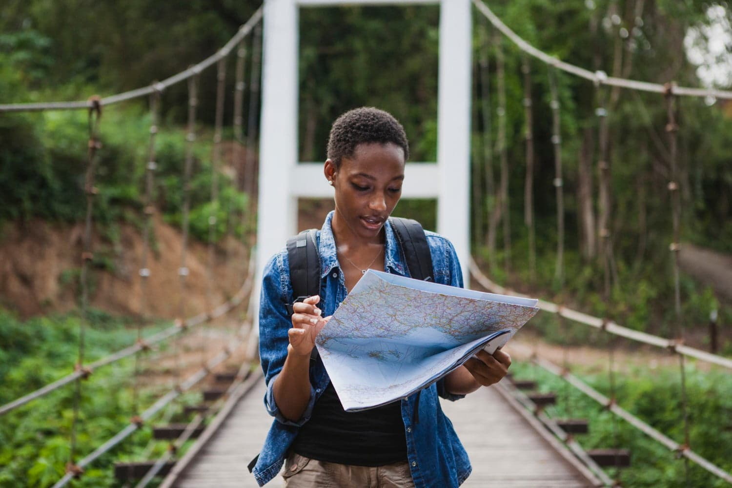 A person stands on a bridge, studying a map surrounded by lush greenery.
