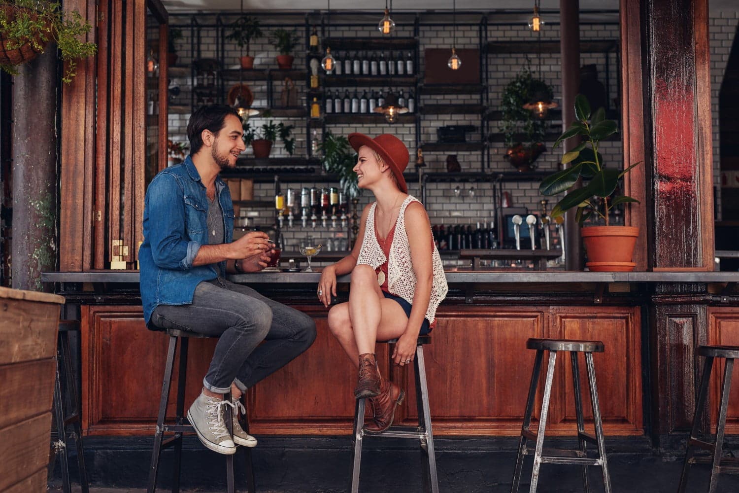A man and woman sit on bar stools at a cafe, engaged in conversation.