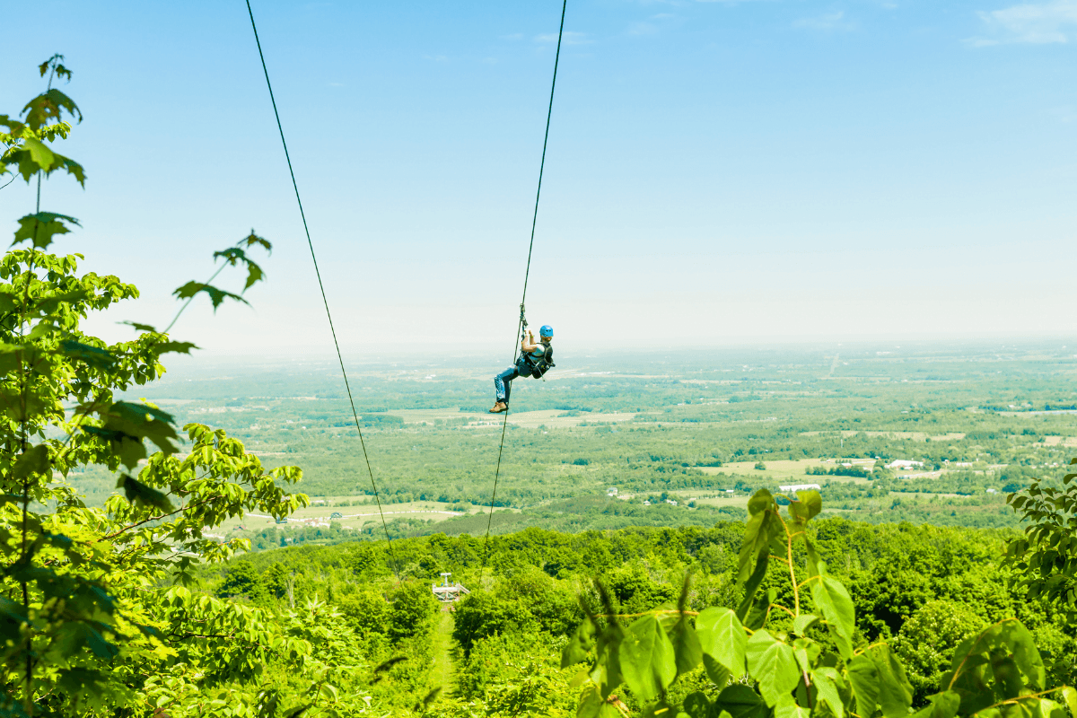 A person ziplining over a lush green landscape under a clear blue sky.