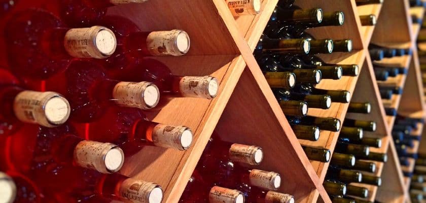 Wine bottles stored in wooden racks with corks facing outward in a warmly lit wine cellar.