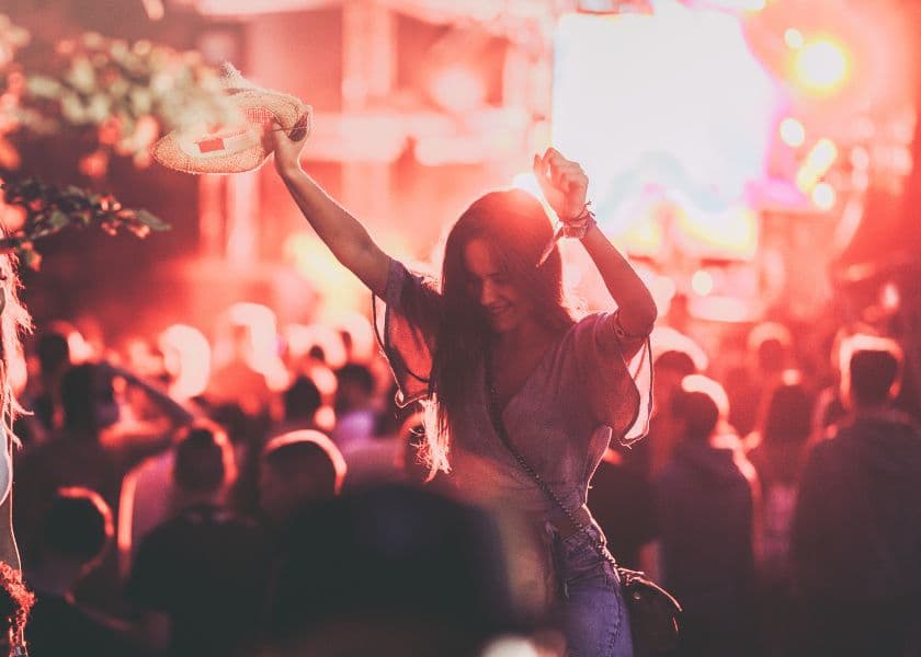 A woman dancing at a lively music festival with bright stage lights in the background.